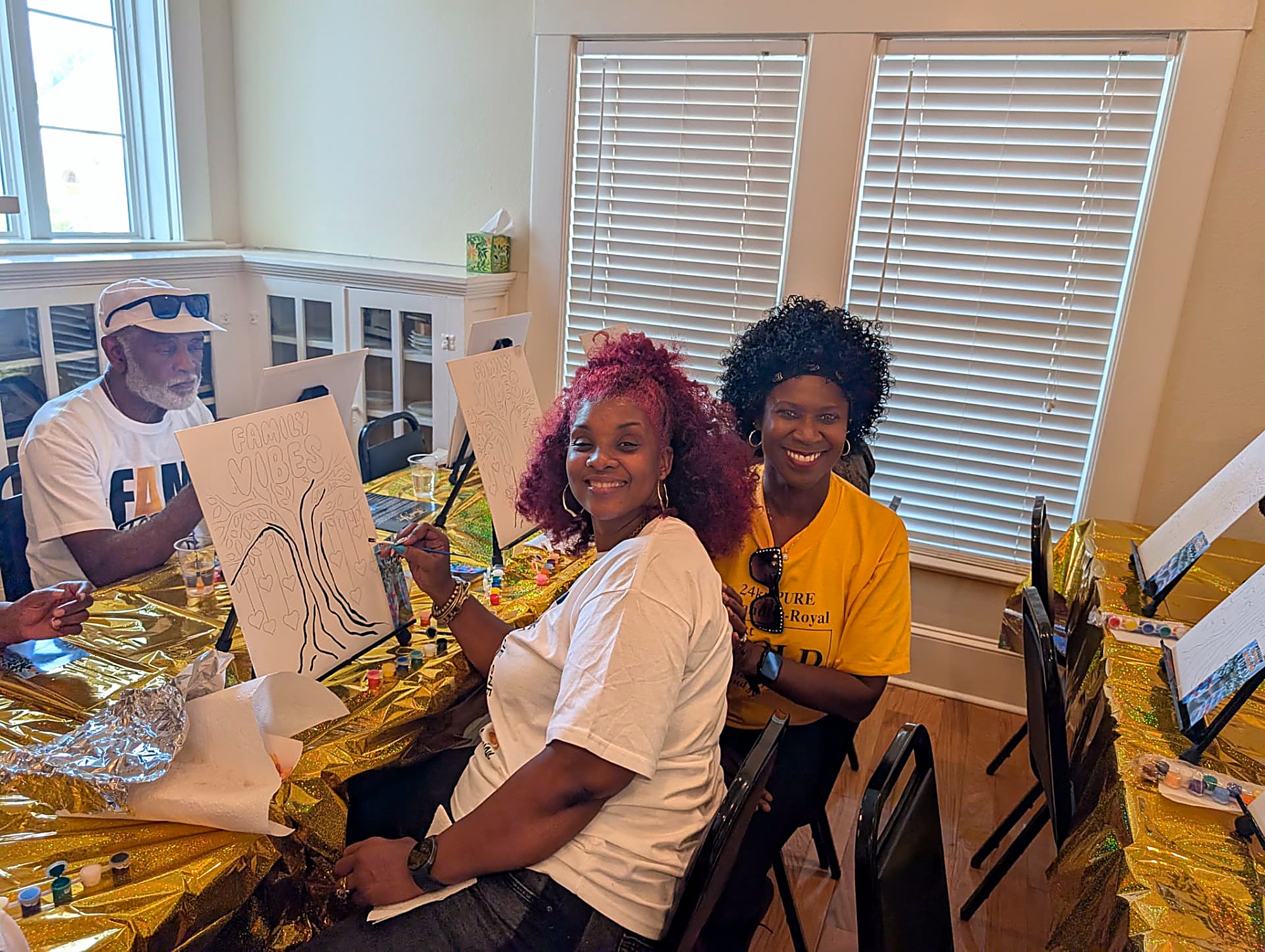 Two cousins smiling over their Family Vibes canvases at the paint party