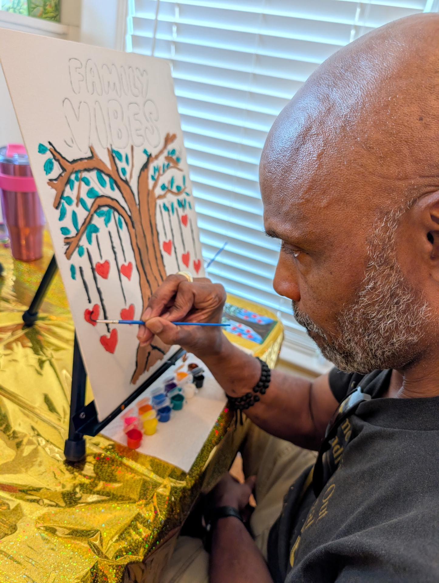 An elder Chandler carefully painting red hearts onto his Family Vibes tree