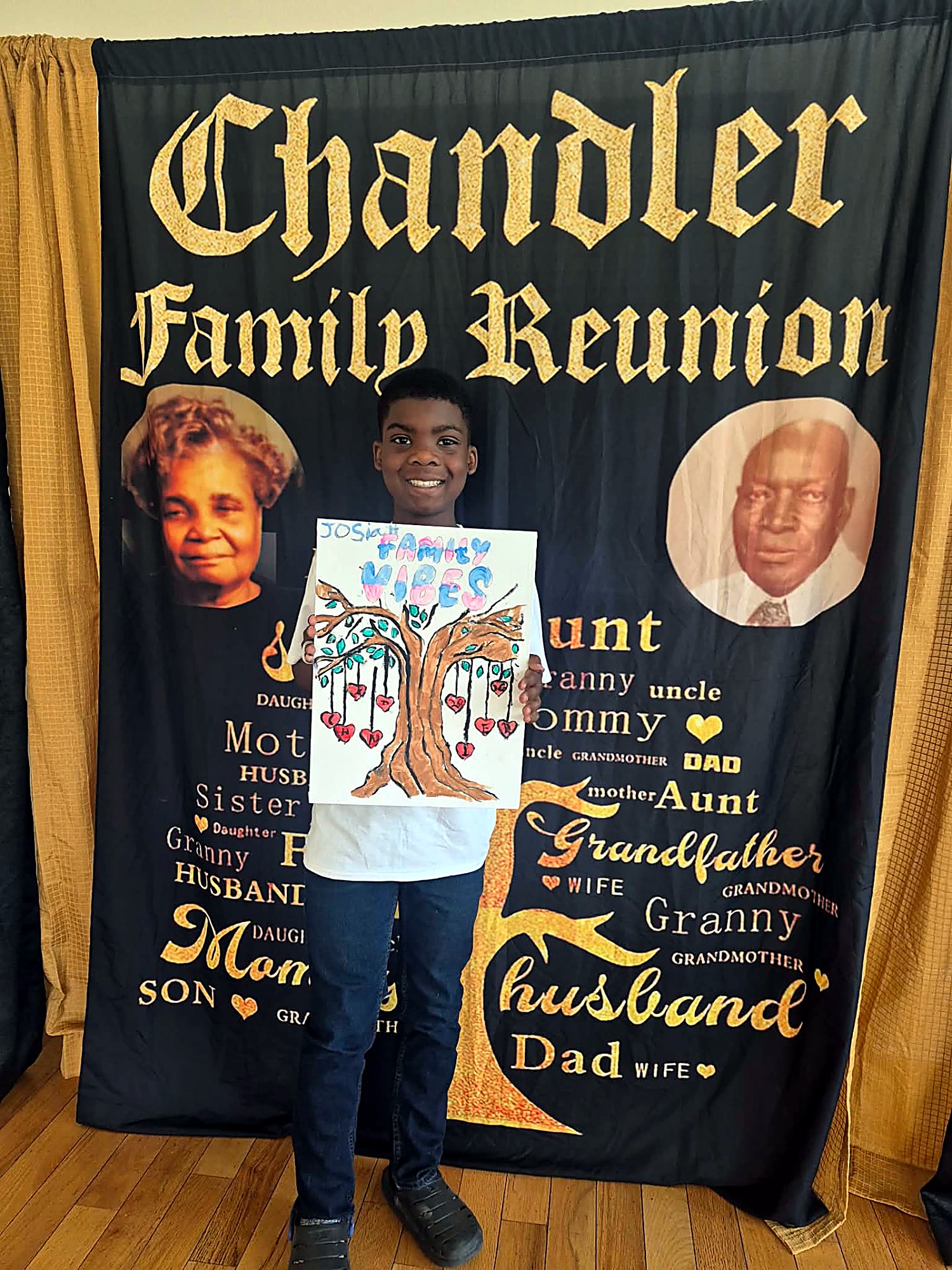 A young Chandler holding up his finished Family Vibes painting in front of the reunion banner